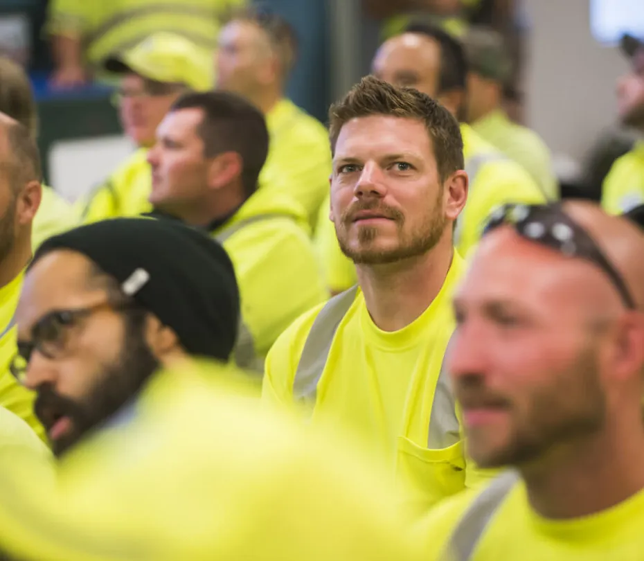 Group of workers in bright yellow safety shirts attending an indoor meeting.