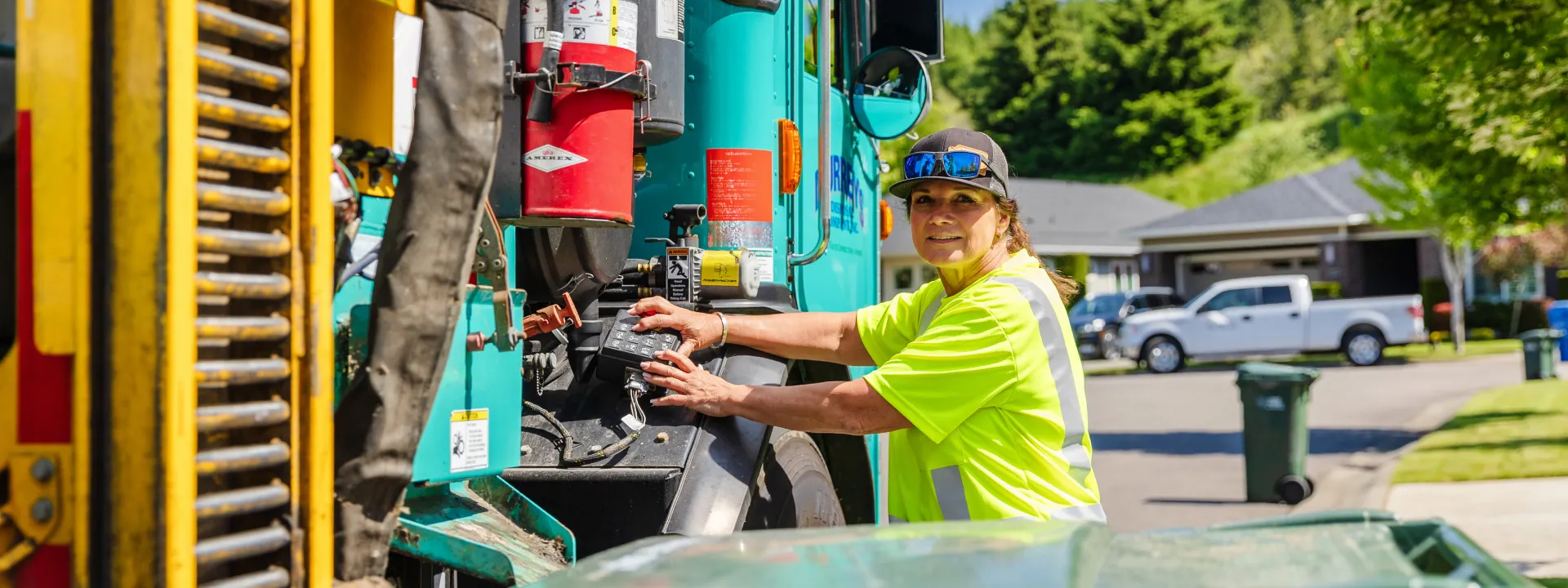 Sanitation worker in fluorescent shirt operating residential garbage truck controls outdoors.