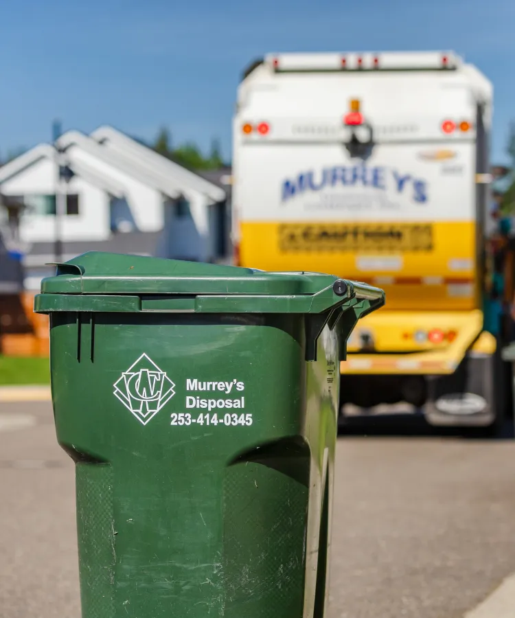 Green curbside trash cart with Murray's Disposal logo and phone, truck blurred in background.