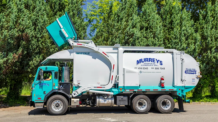 Front-load garbage truck lifting a dumpster with Murrey's Disposal signage on a sunny day.
