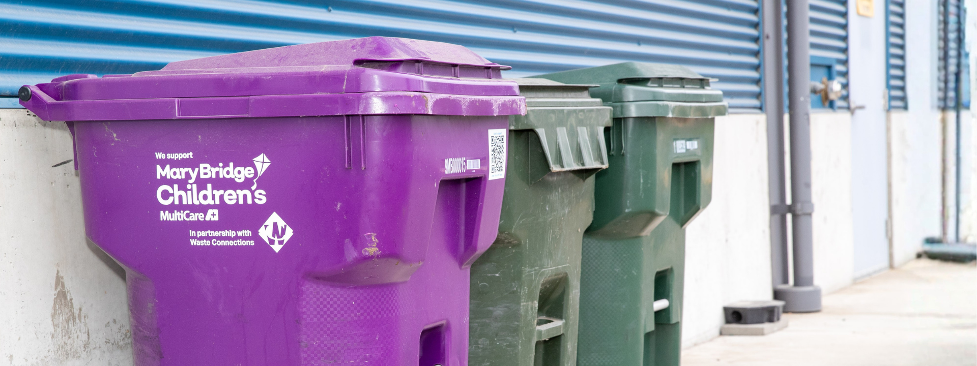 Row of three outdoor waste bins, with a prominent purple bin supporting Mary Bridge Children’s hospital.