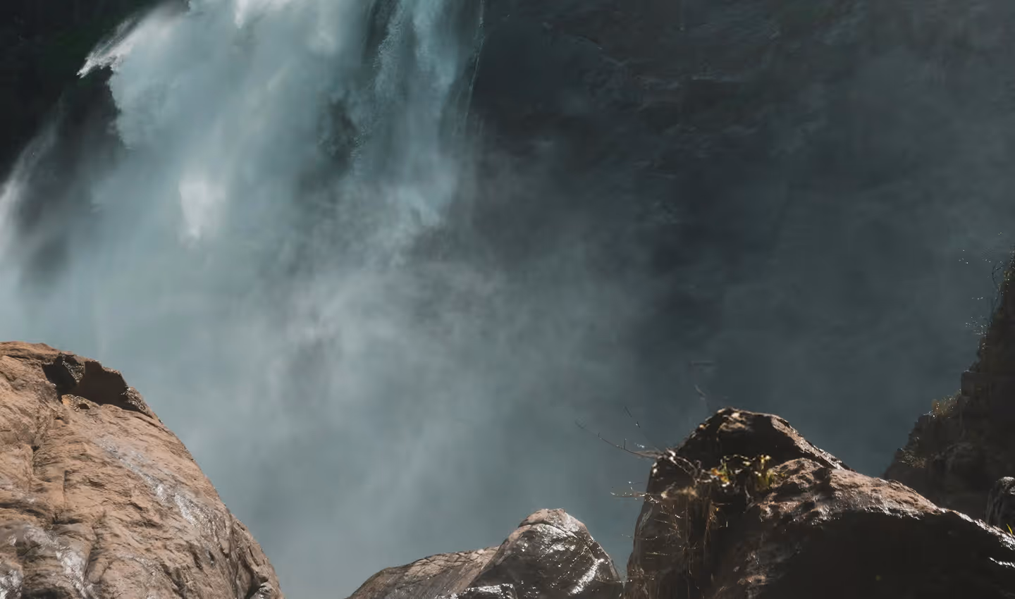 View of water cascading down a rocky waterfall with mist rising above wet stones.
