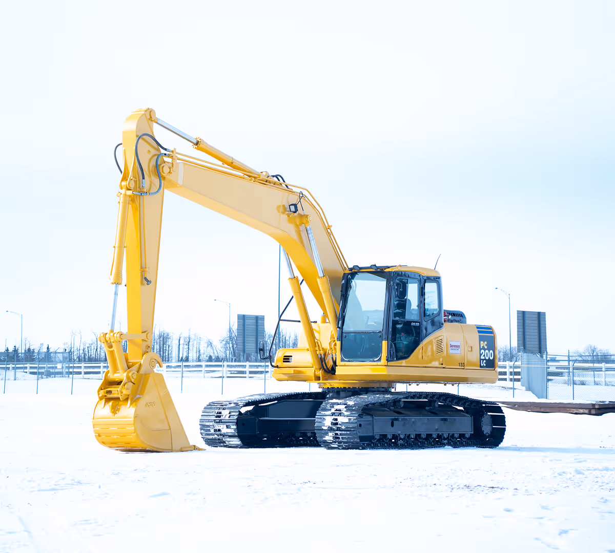 Yellow Komatsu PC200 LC excavator on snow-covered ground with a clear sky background.