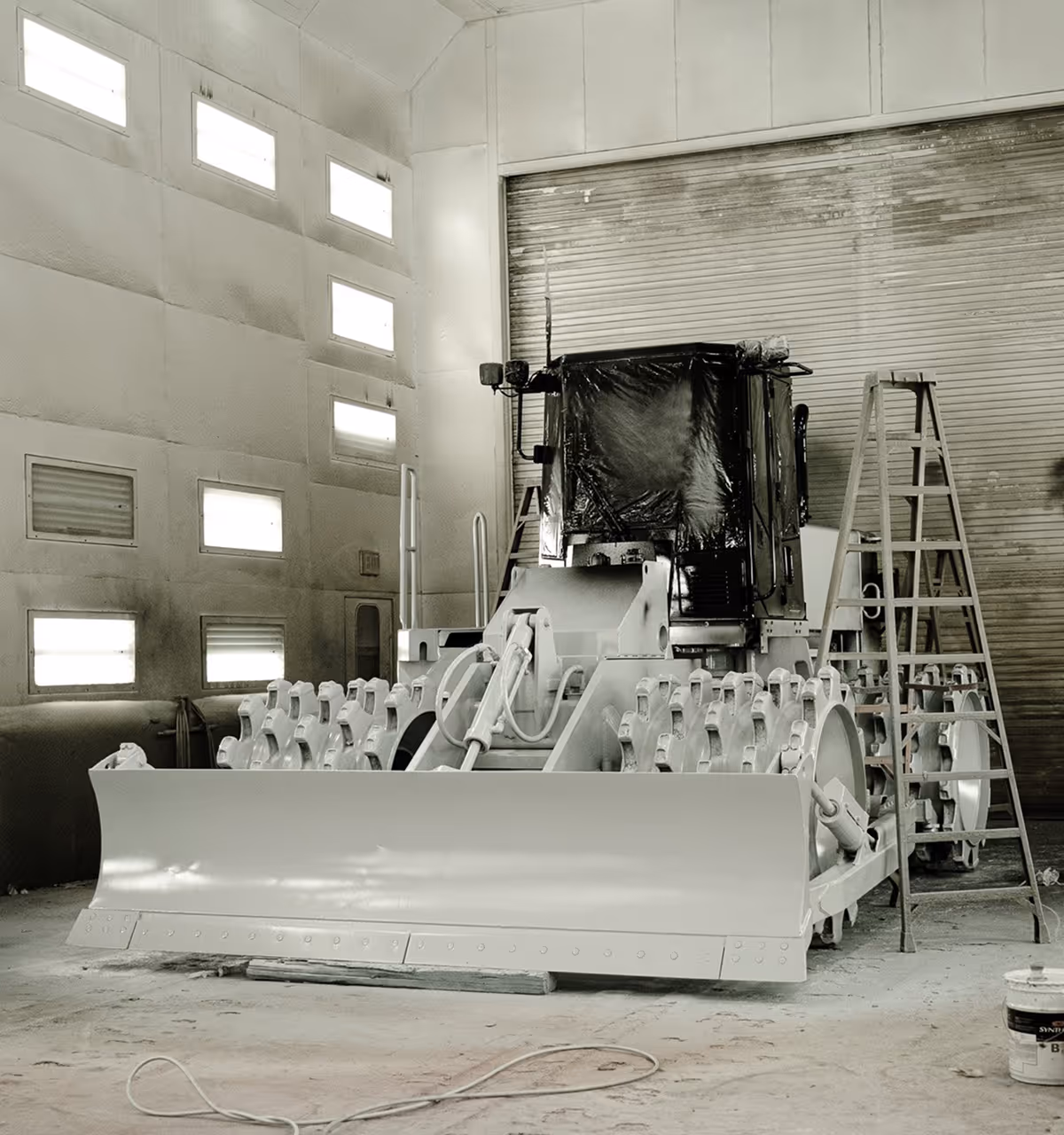 Large bulldozer with a wide blade in an industrial workshop with ladders nearby.