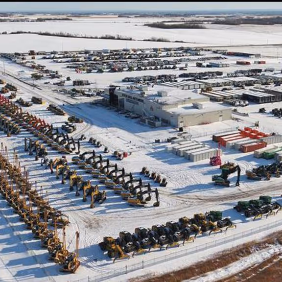 Aerial view of a snowy industrial yard with numerous construction vehicles and equipment parked in rows.