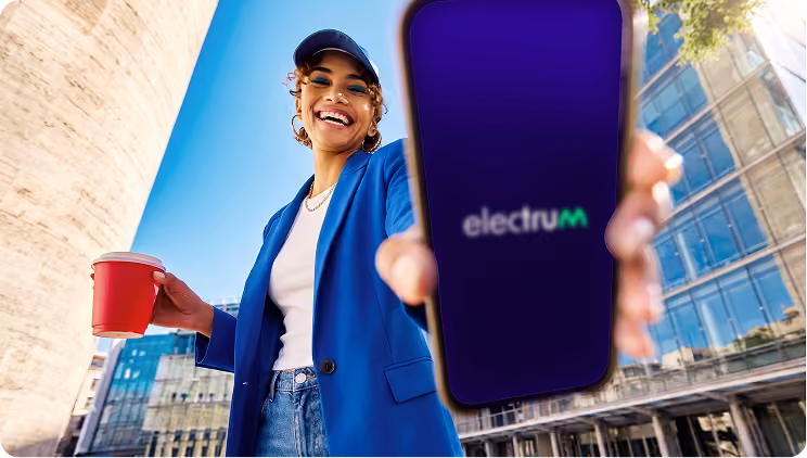 Smiling woman holding a red cup and showing a phone screen with Electrum app logo outdoors.