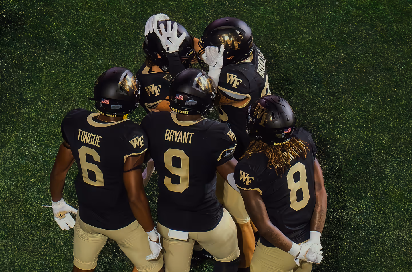 Three American football players in green uniforms and white helmets huddled together under dramatic blue smoky stadium lighting