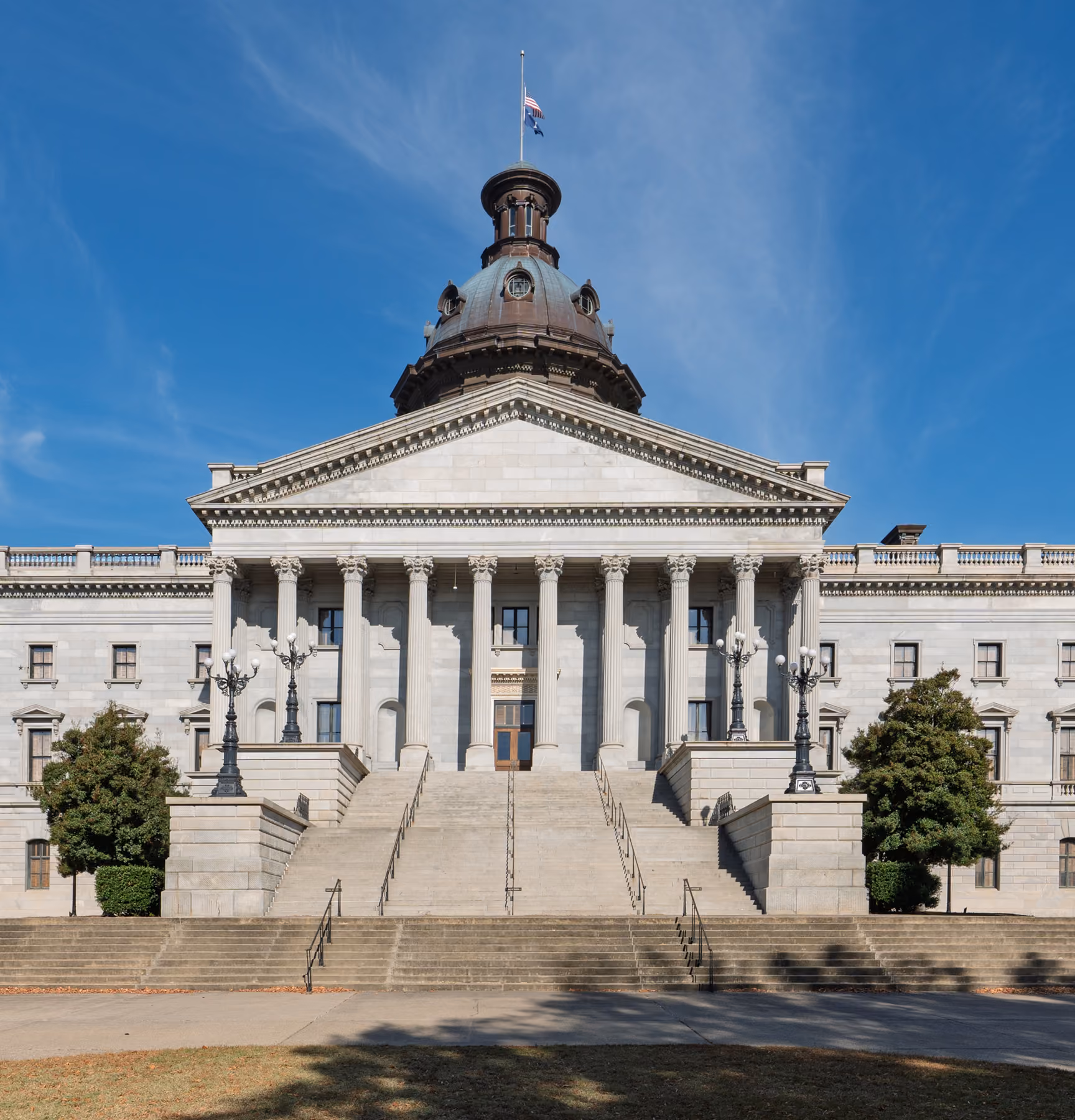 Front view of a classical government building with tall columns and staircases under a blue sky.