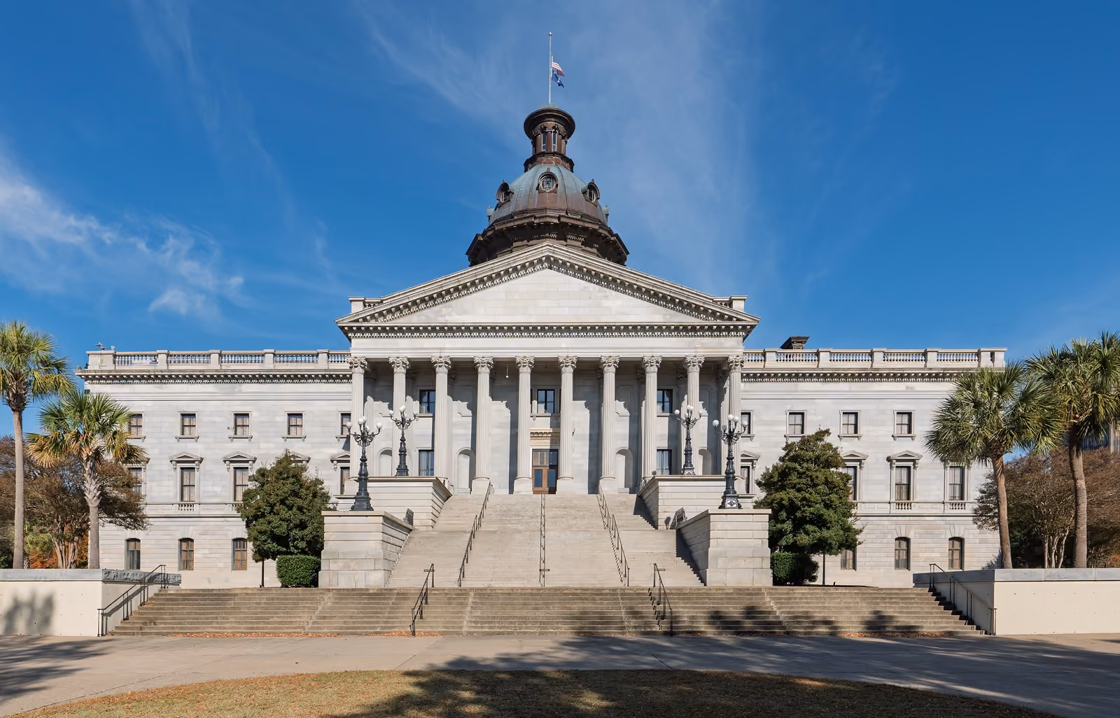 Front view of a white neoclassical government building with columns, stairs, dome, and flags.