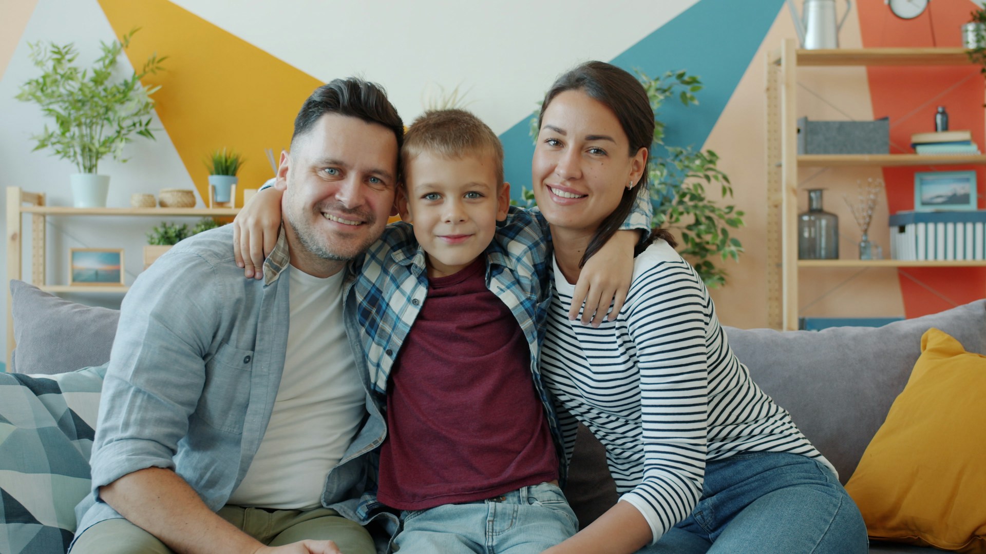 A family of three smiling at the camera, sitting on a couch