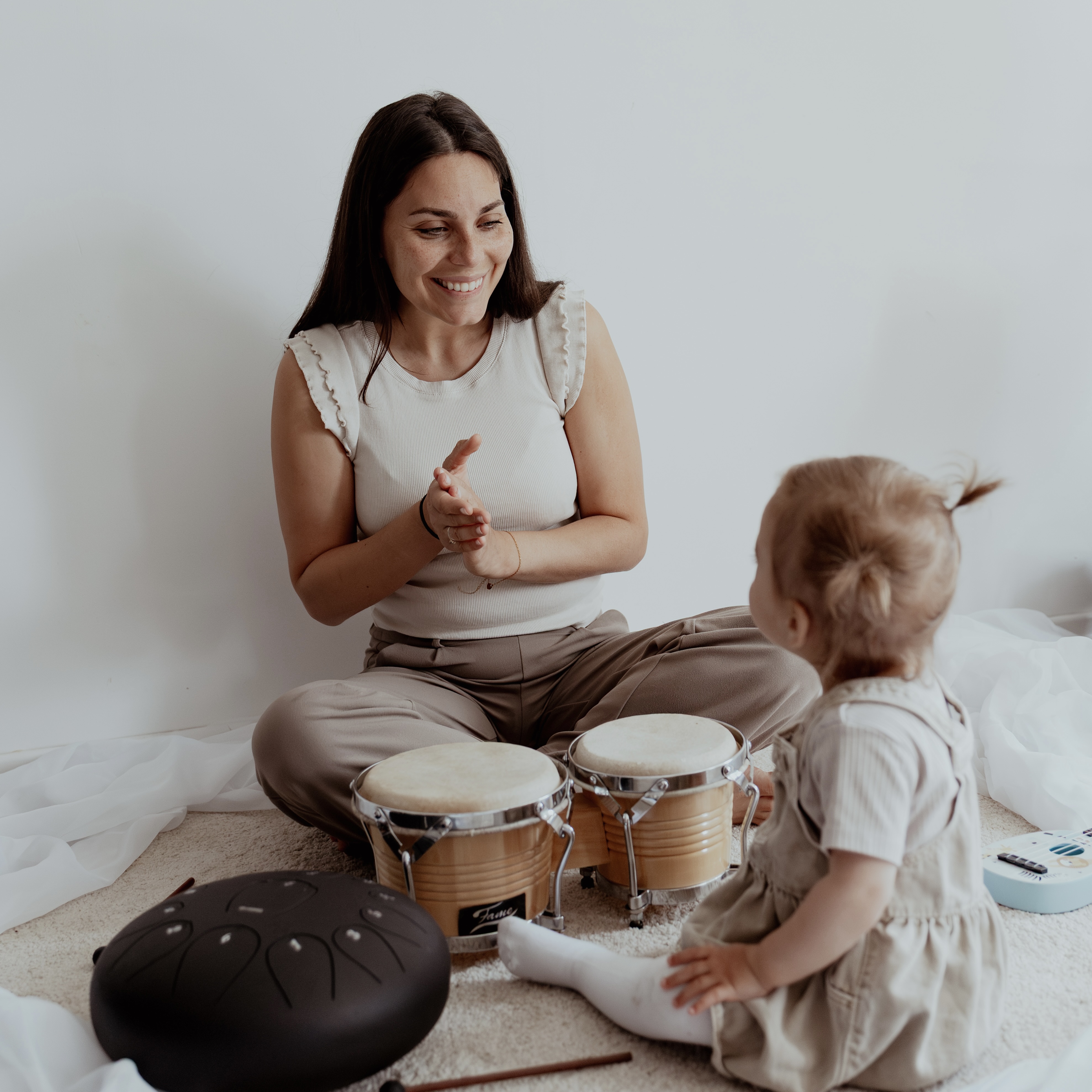 Caro Reddmann interagiert fröhlich mit kleinem Mädchen zwischen Trommeln und weiteren Musik Instrumenten