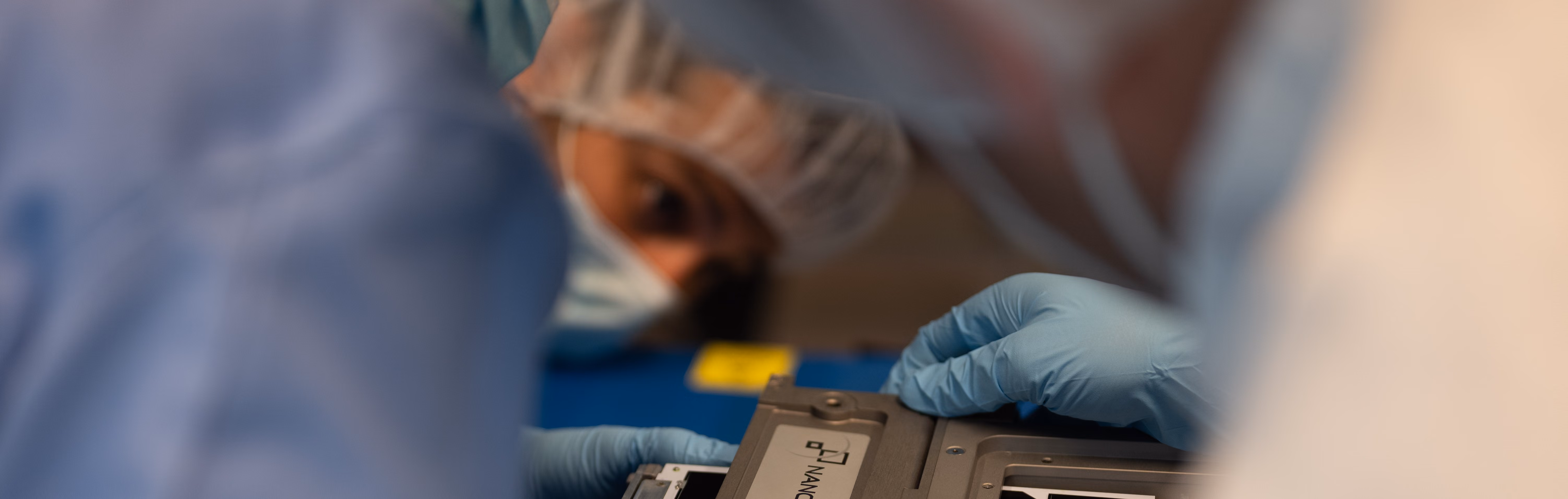 Person in lab coat and gloves handling a device labeled Nanopore in a lab setting.