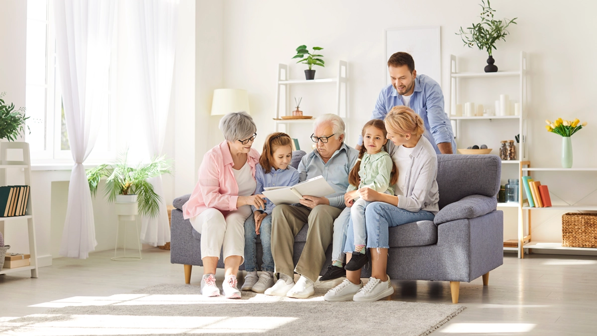Multigenerational family sitting on sofa reading a book in a bright, cozy living room.