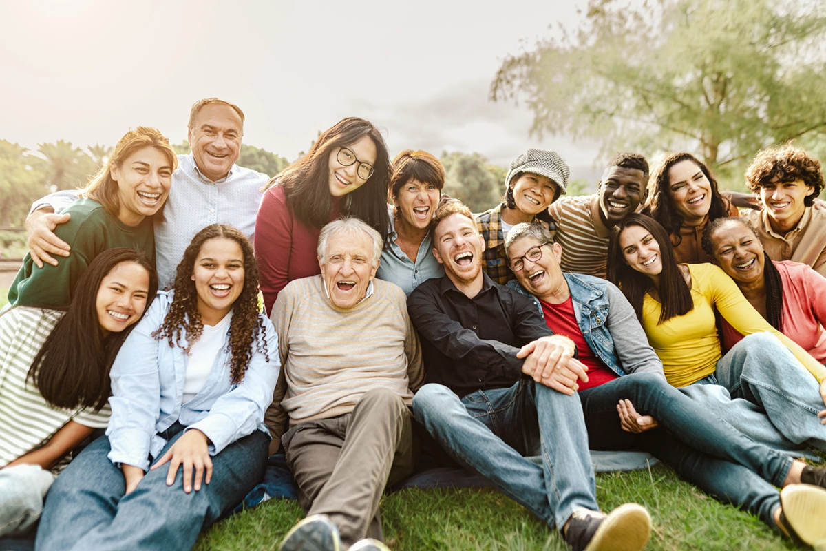 Group of diverse people sitting on grass outdoors, smiling and laughing together.