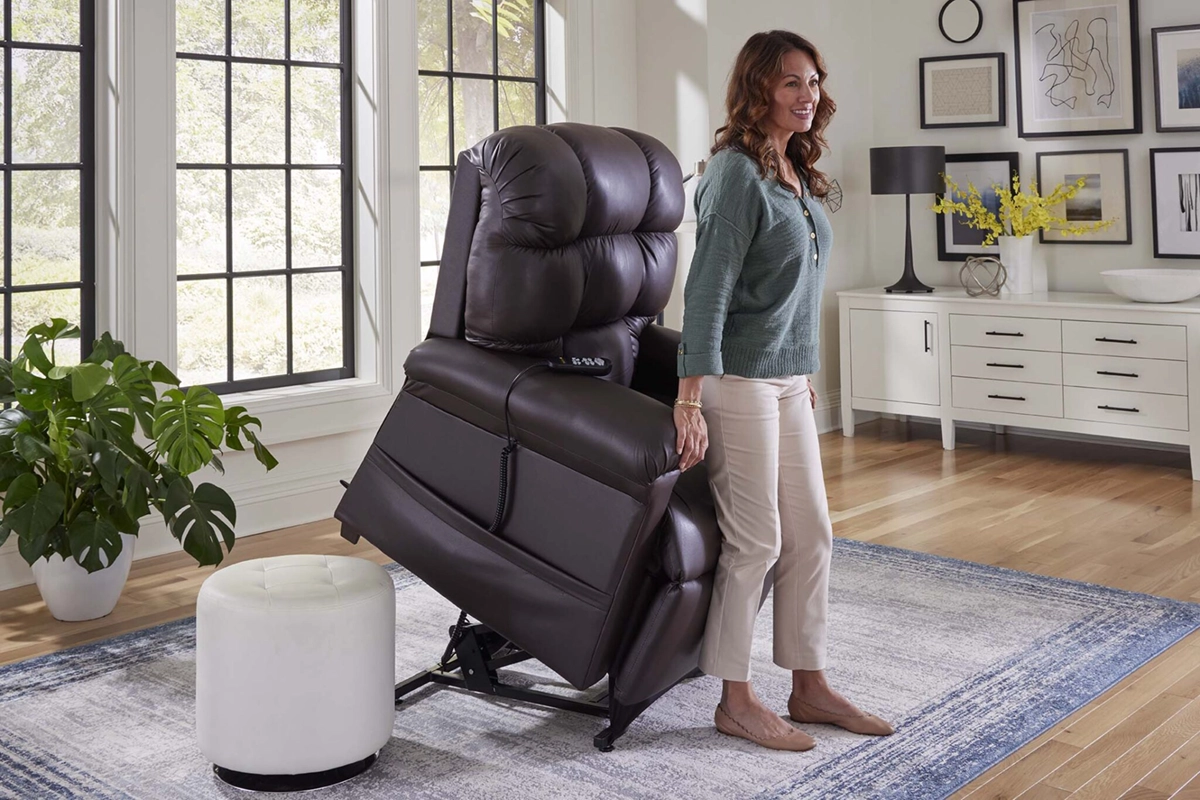 Woman standing beside a raised dark brown recliner chair in a bright living room.