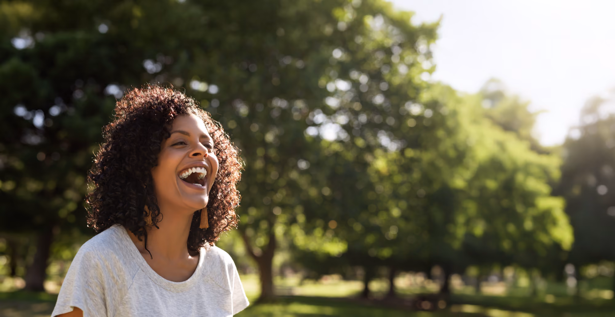 Woman laughing outdoors among trees.