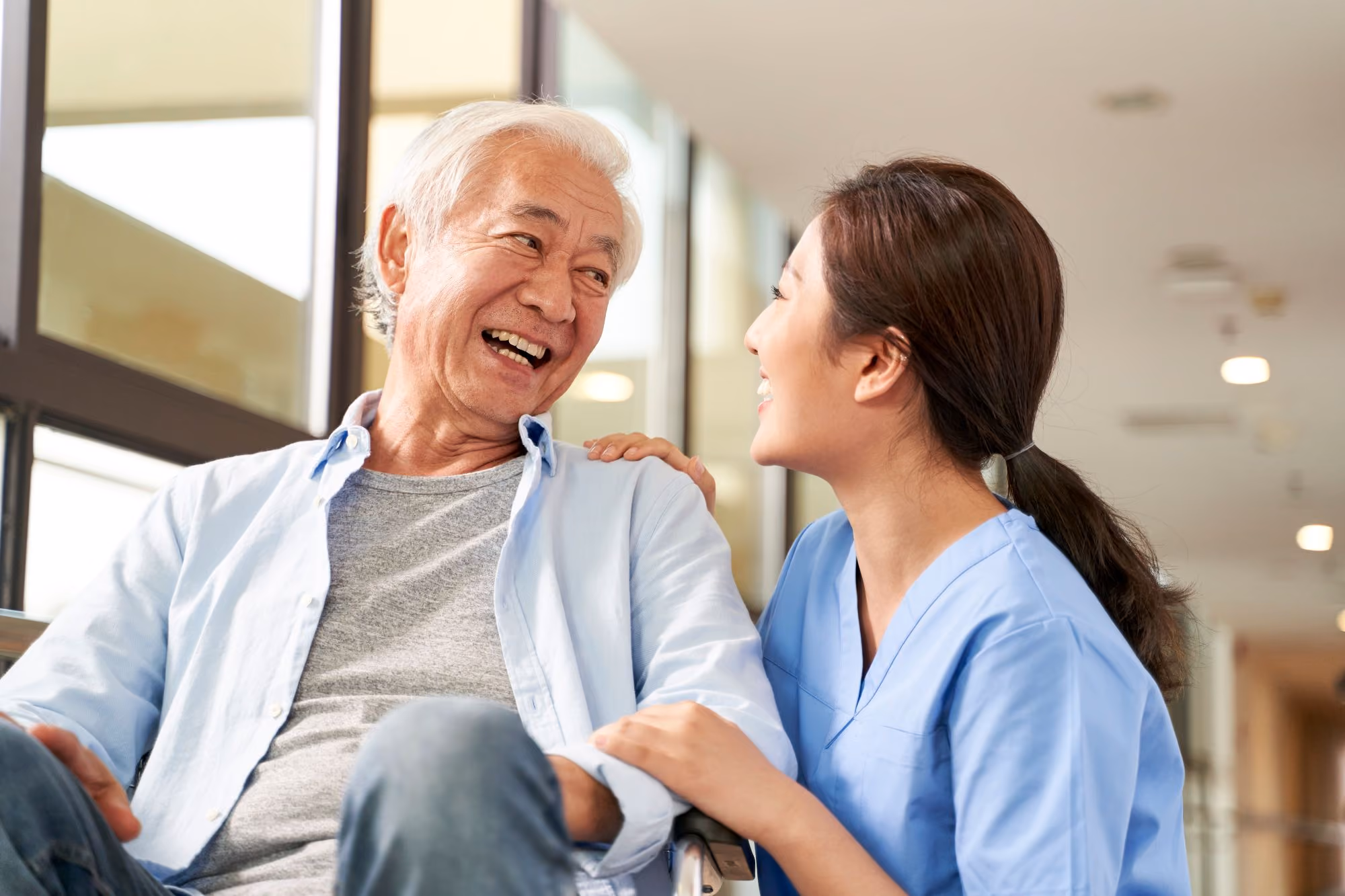Health care provider in scrubs laughing with an older man.