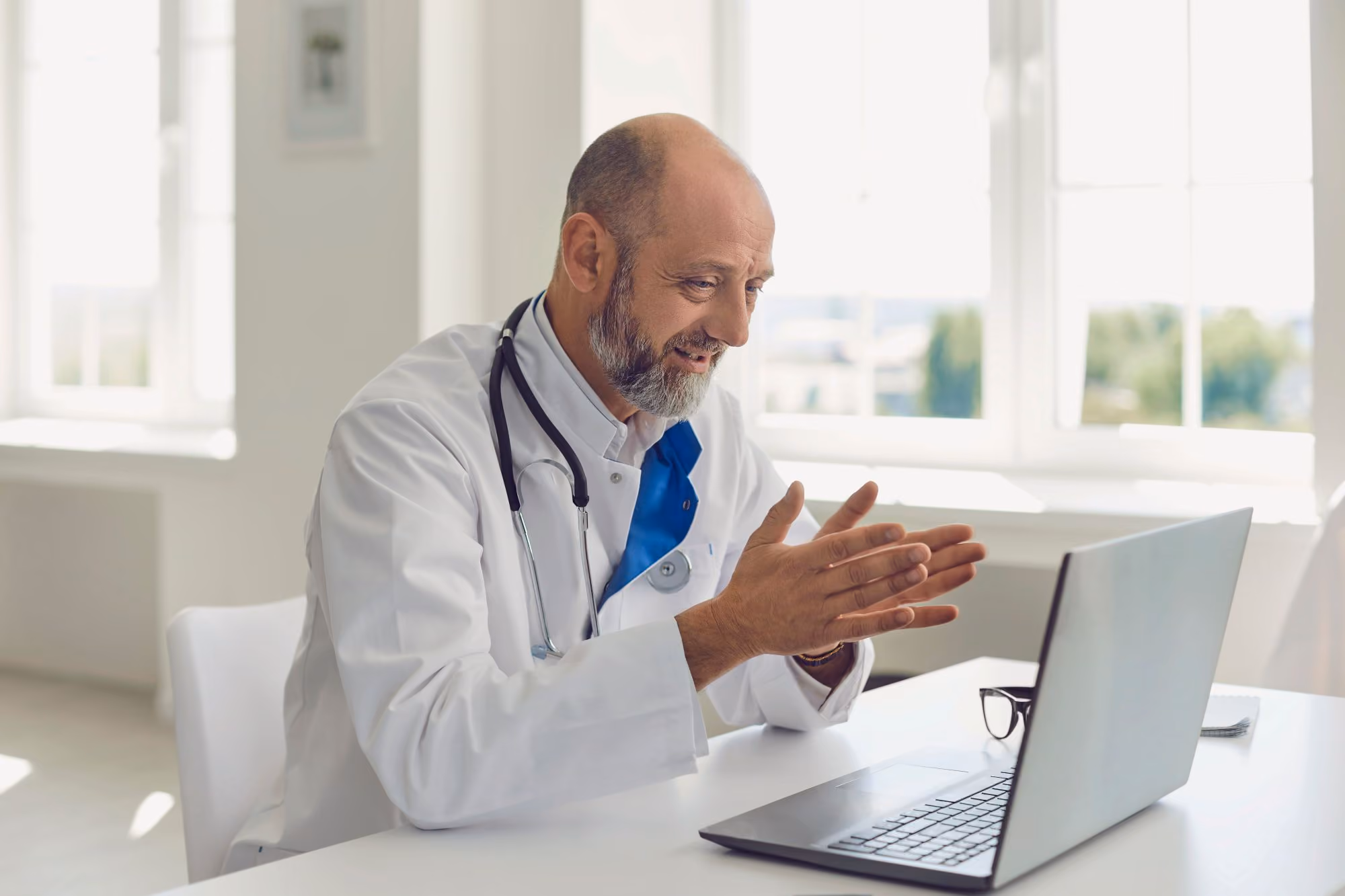 Doctor in a white coat gesturing while talking at a laptop