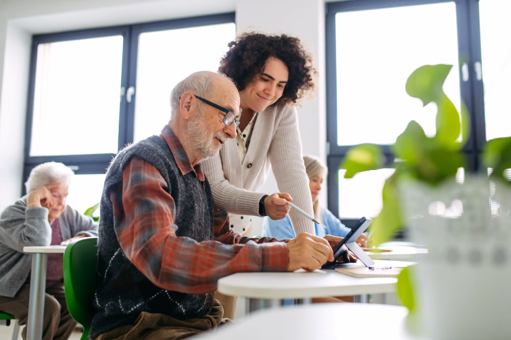 Woman helping an older man with a tablet in a classroom.