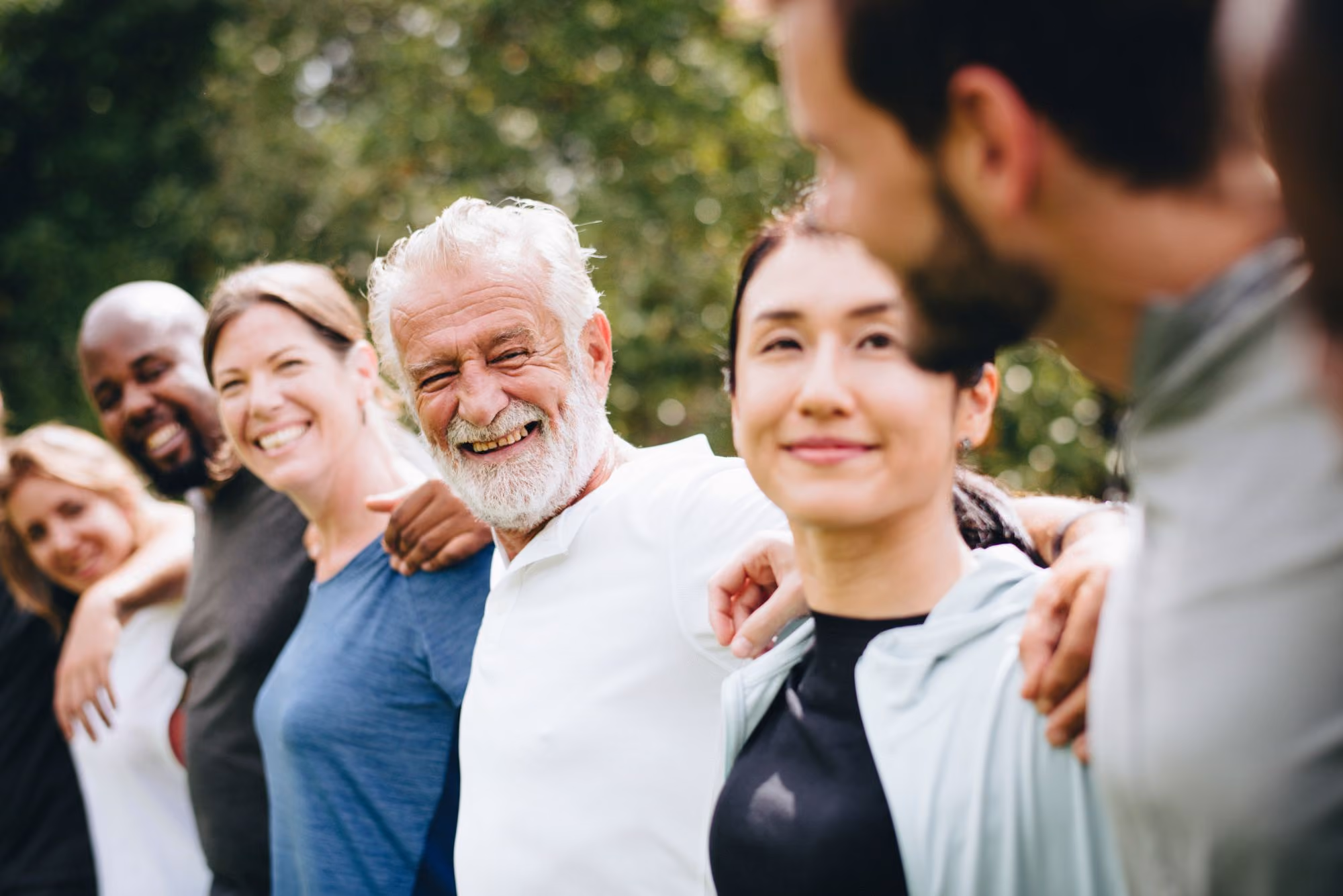 Group of people standing outdoors with arms around each other, smiling.