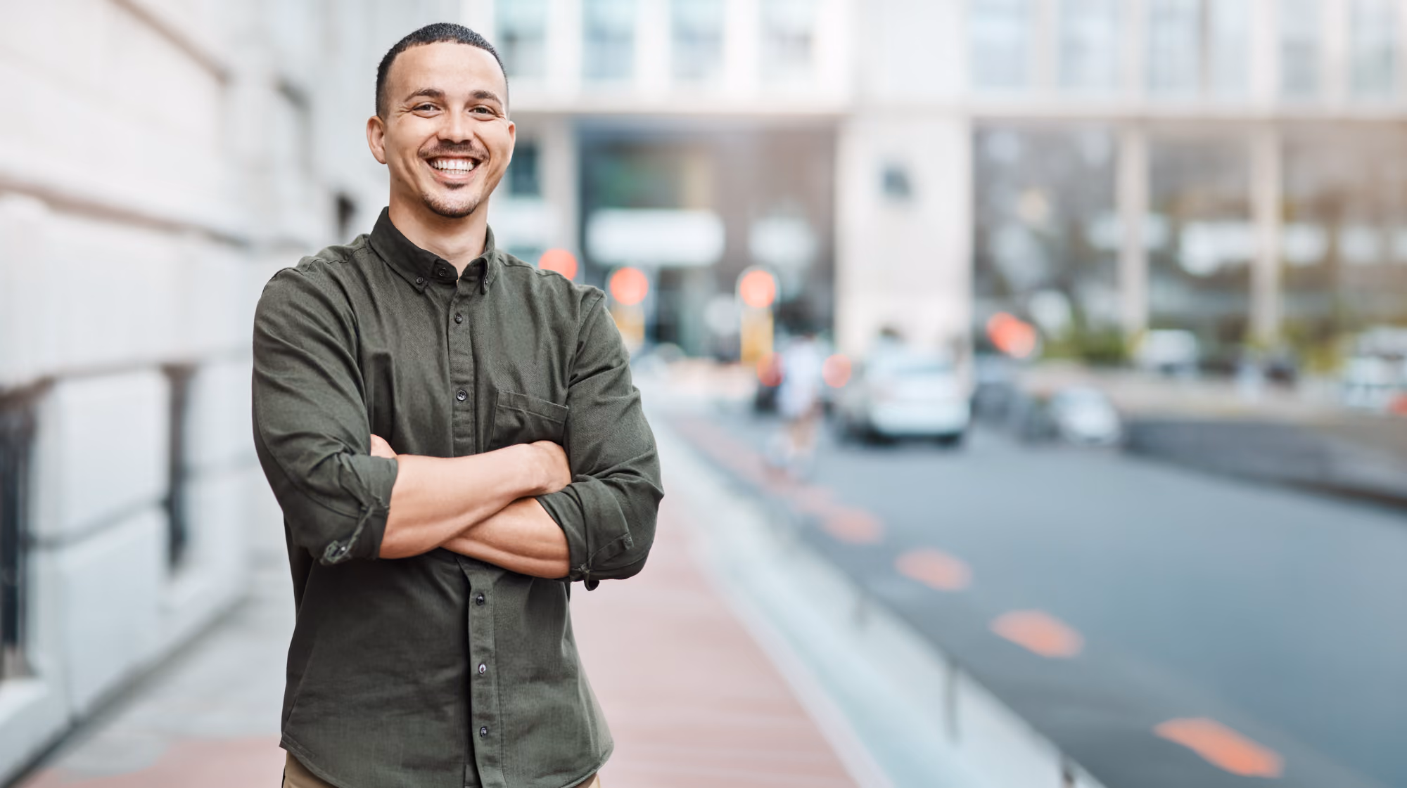 Man standing with arms crossed outdoors, smiling.