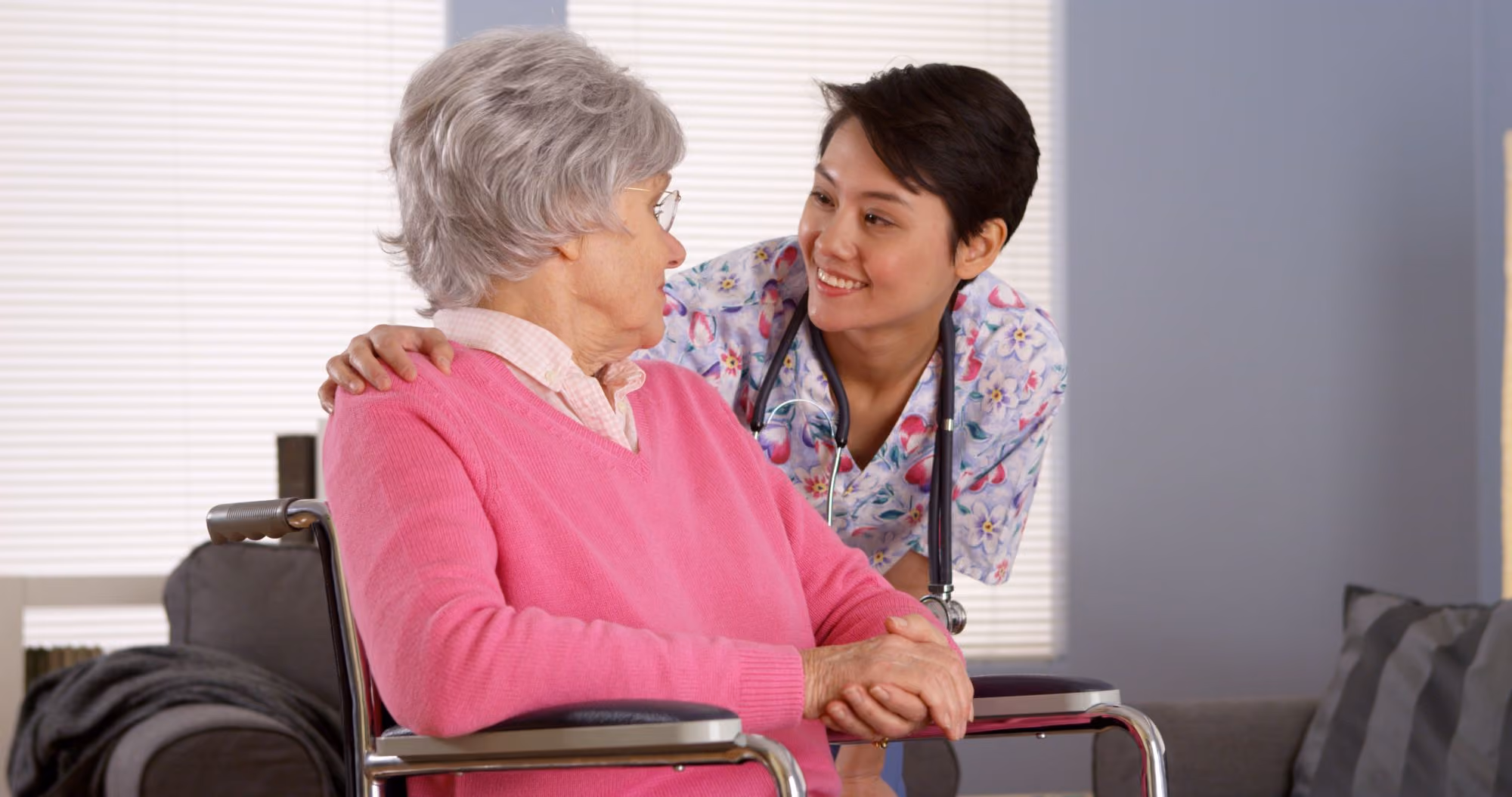 Nurse in scrubs smiling with an older woman in a wheelchair.