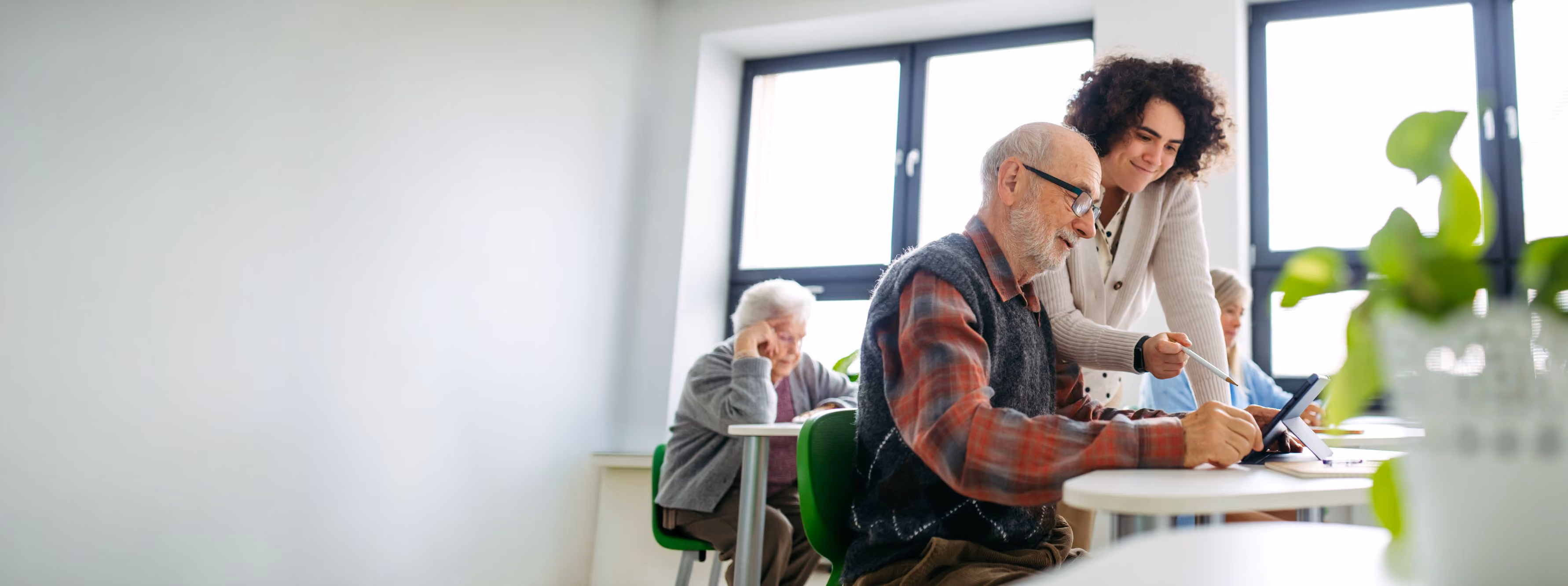 Woman helping an older man with a tablet in a classroom.