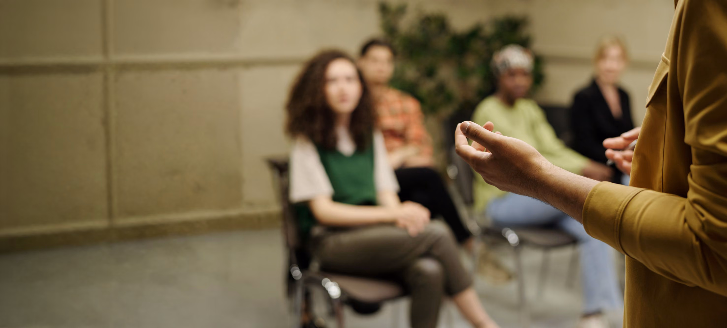 Person gesturing while speaking to a seated group.