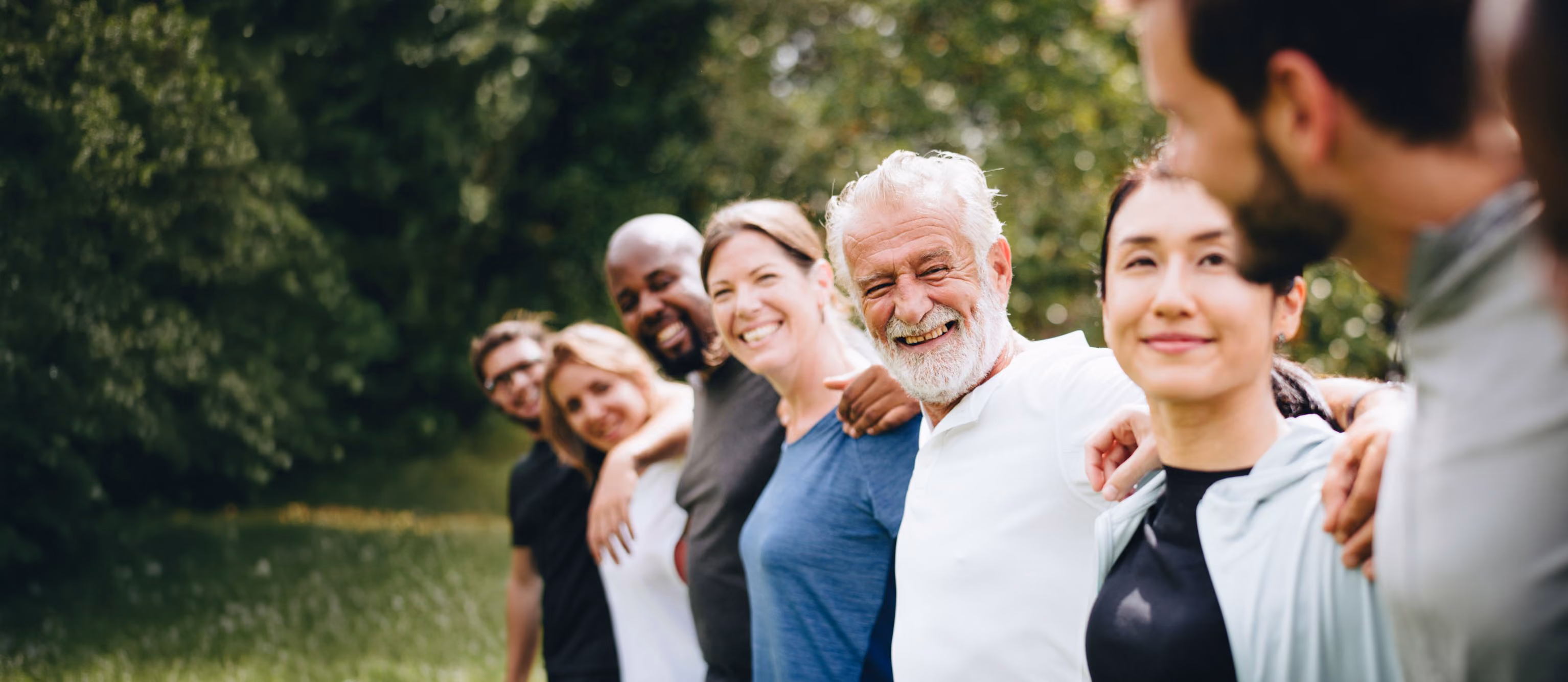 Group of people standing outdoors with arms around each other, smiling.