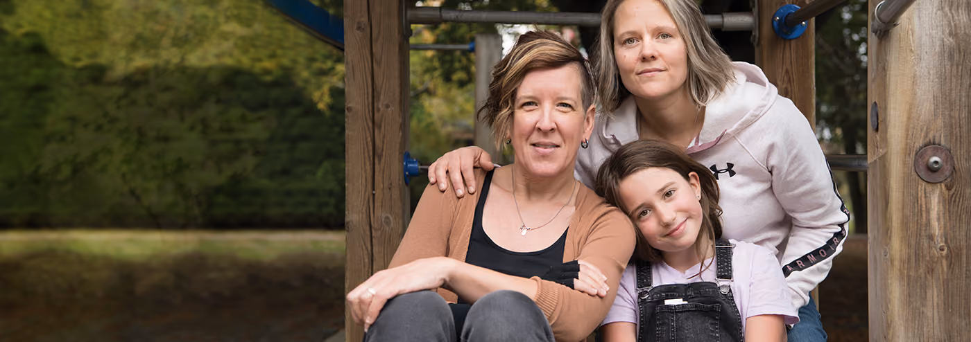 Two women and a child sitting close together on a playground structure.