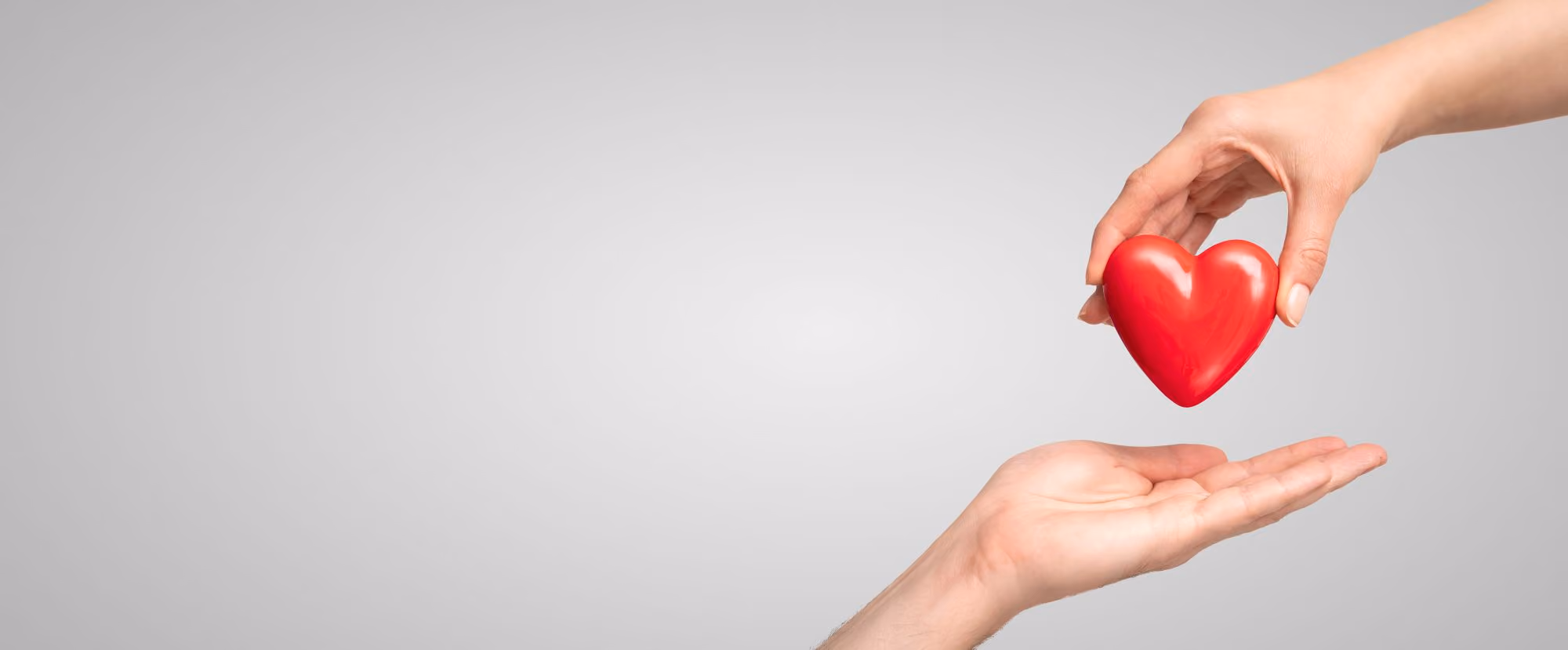 Hand passing a red heart to an open hand below