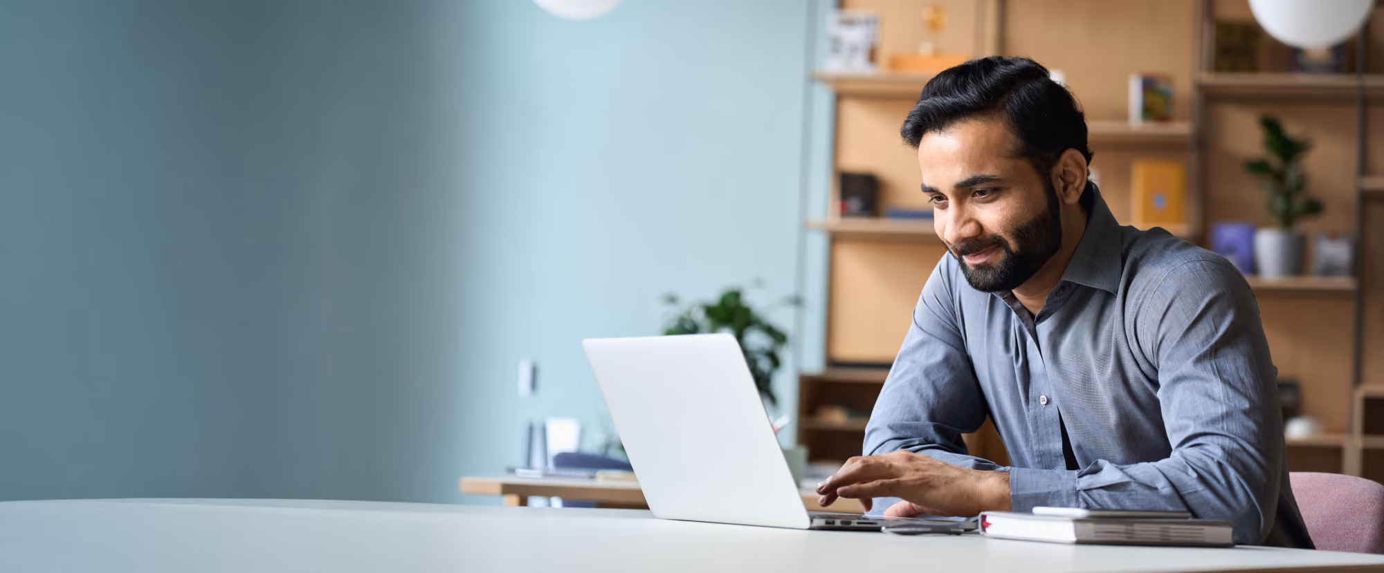 Man working at a laptop in a home office, smiling.