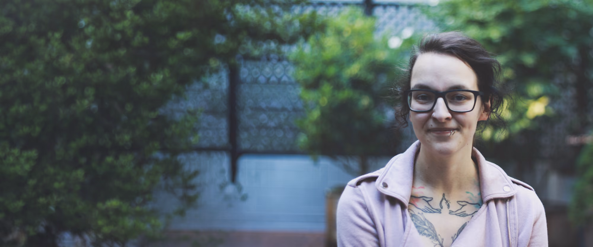 Woman with glasses standing outdoors, smiling.