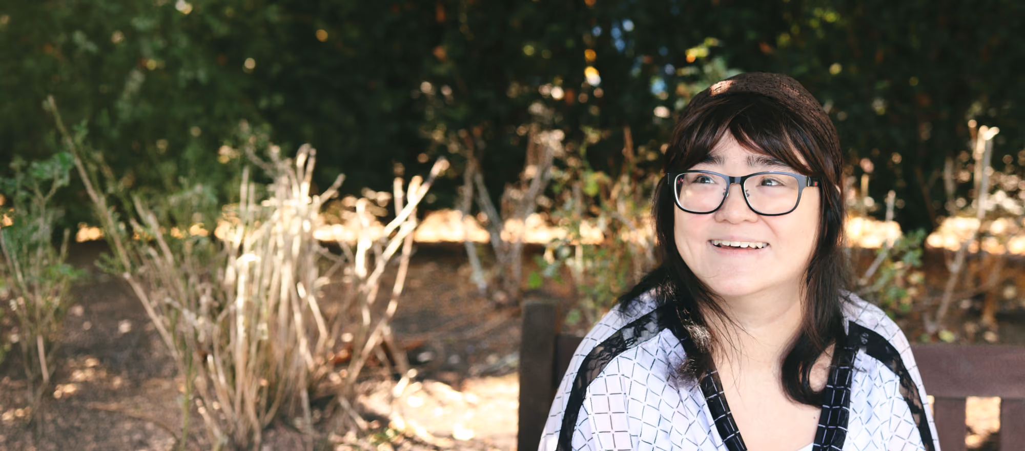 Woman with glasses standing outdoors, smiling.
