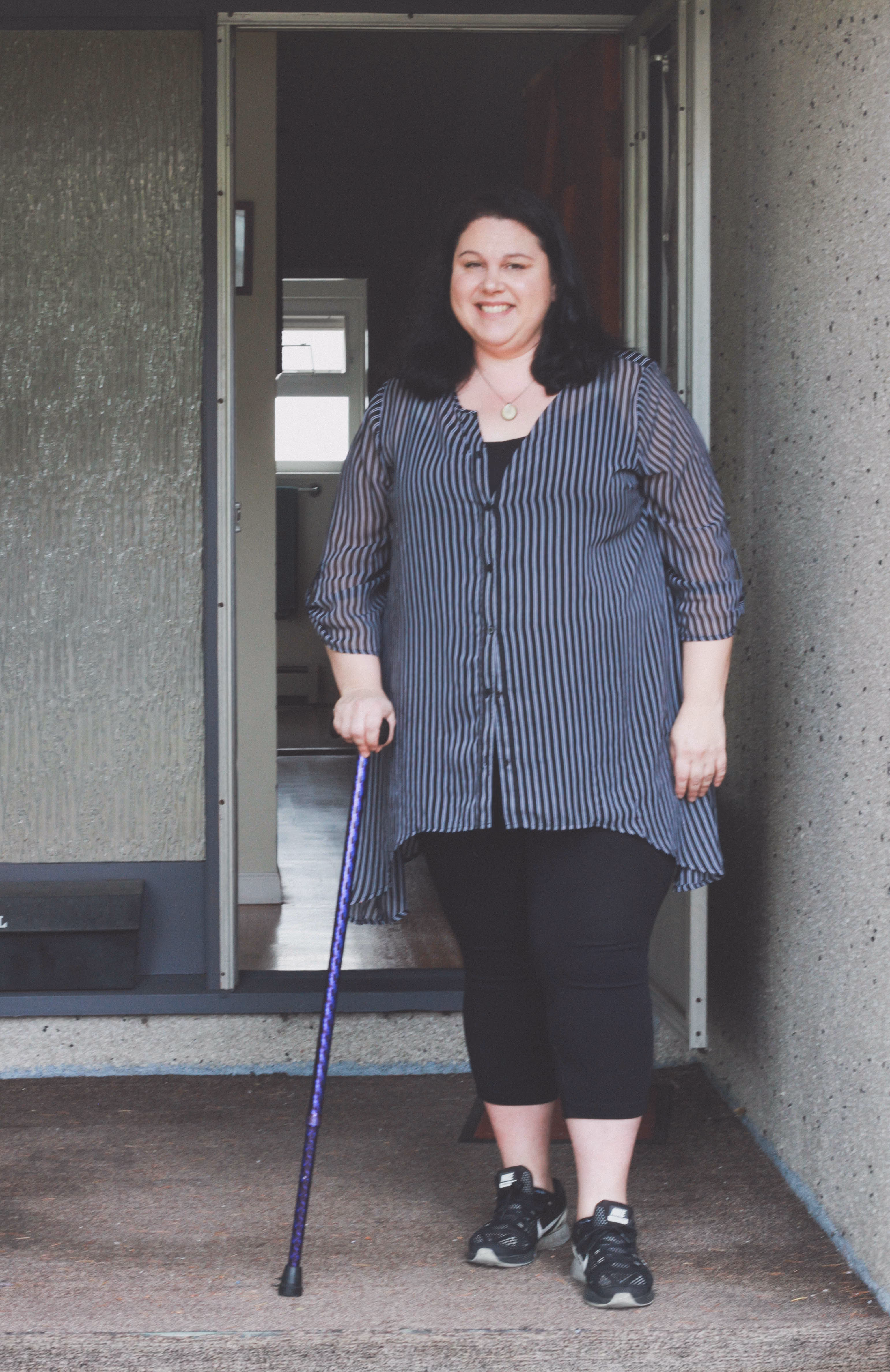 Woman standing in a doorway with a cane.