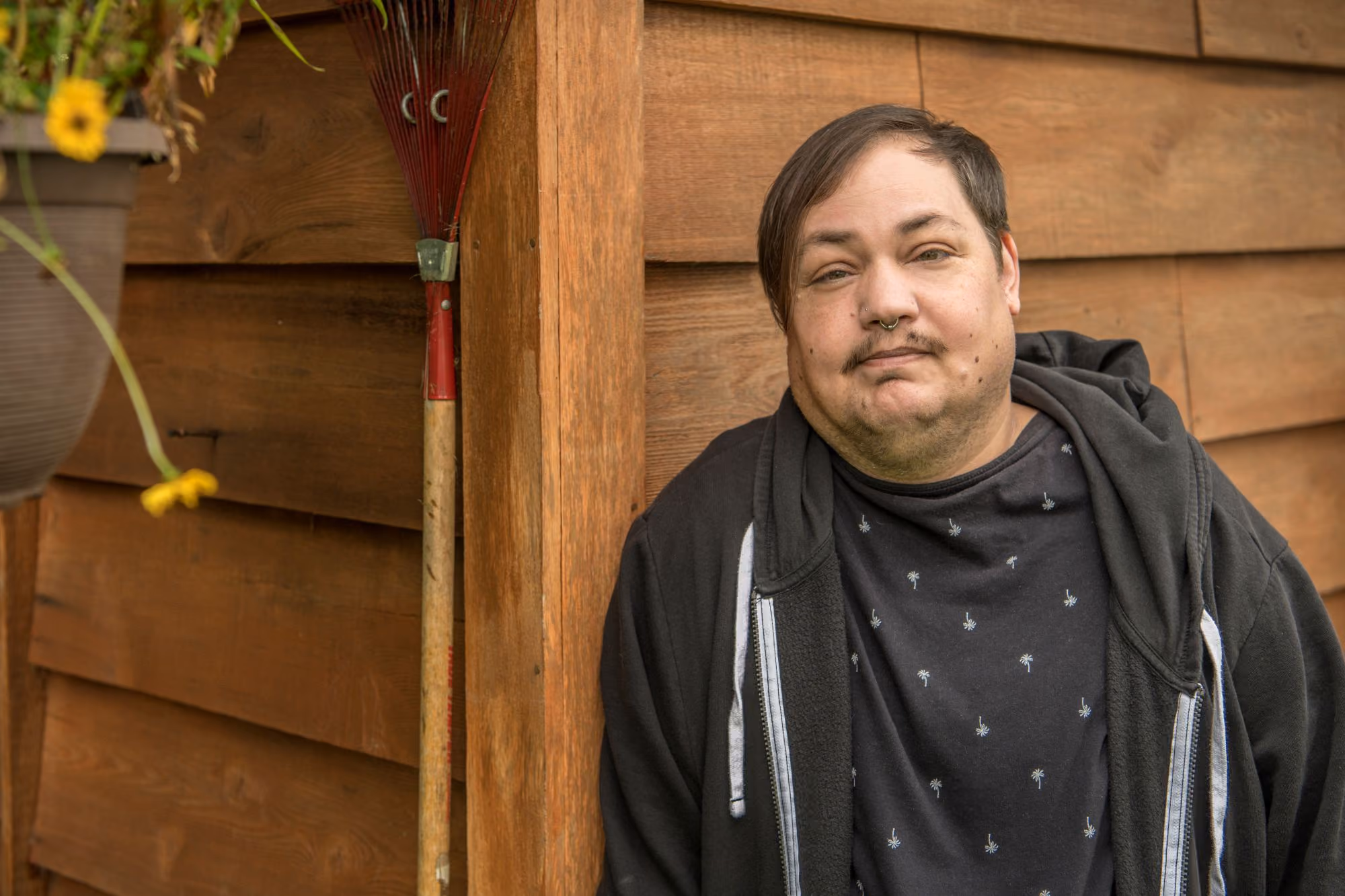 Man leaning against a wooden wall, smiling.