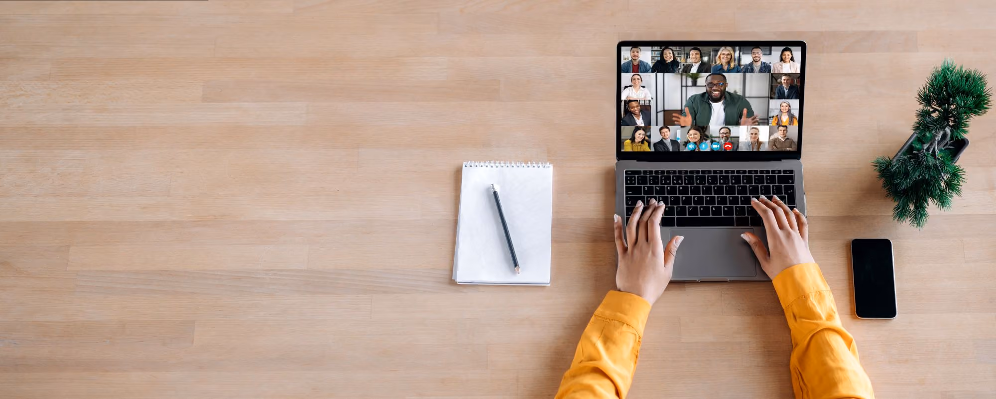Overhead view of hands at a laptop showing a video call with many participants.