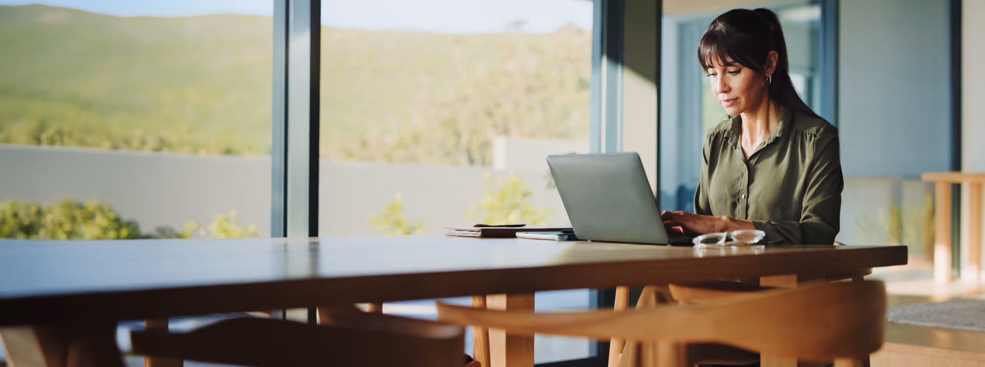 Woman working at a laptop by a window.