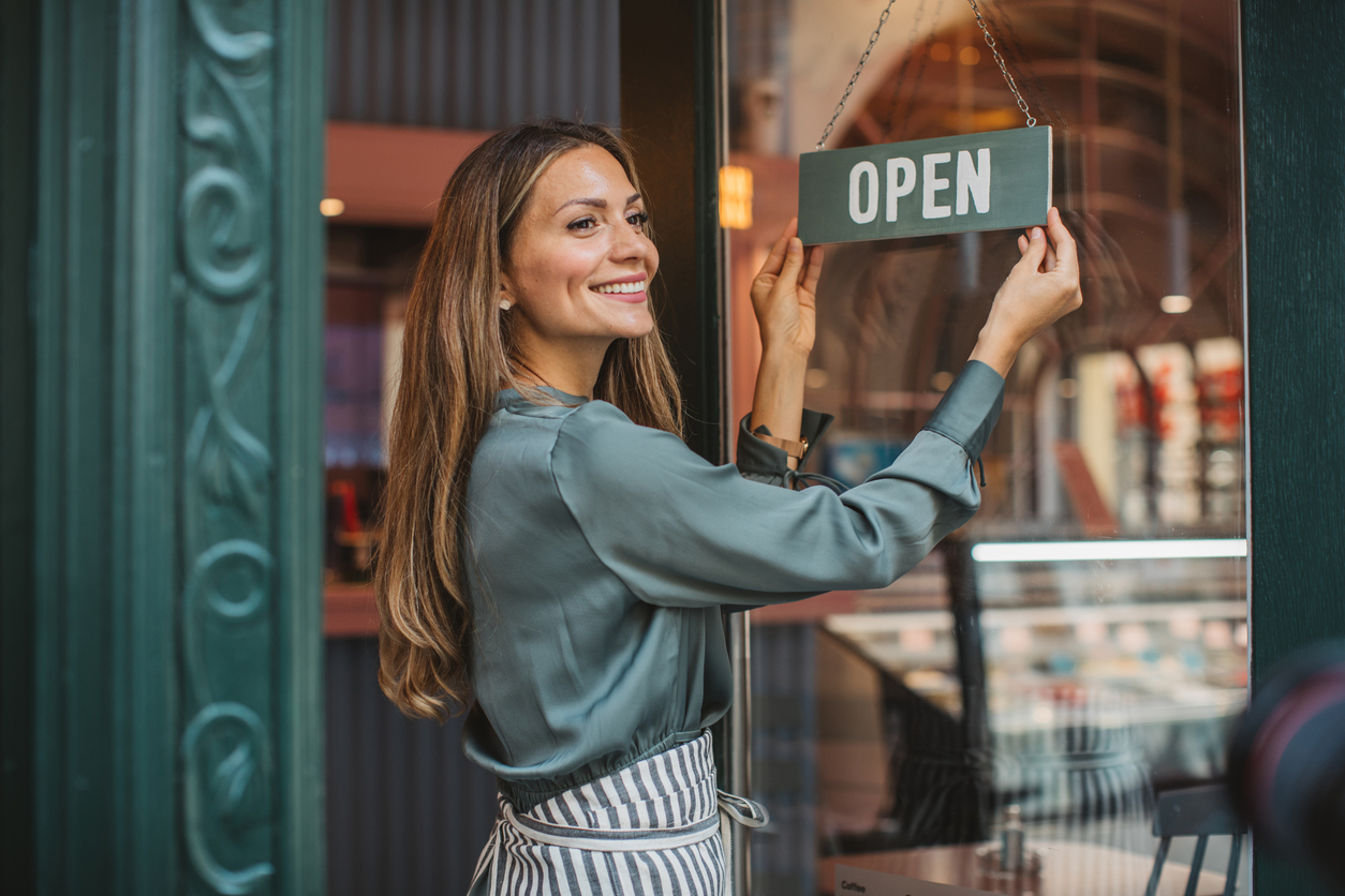 Small business owner smiling as she hangs an "open" sign on her cafe door.