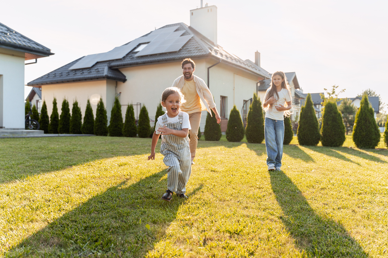 Family runs joyfully in the sunshine in their front yard.