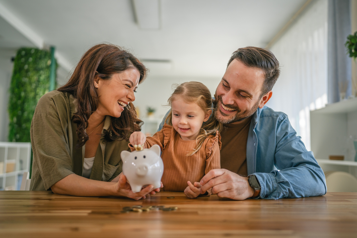 Mother and Father show their daughter how to put coins in a piggy bank.