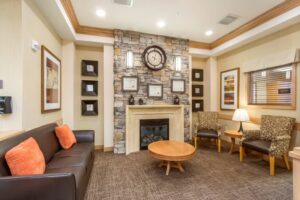 Cozy lobby area of Chelsea Place in Aurora, CO, featuring a stone fireplace, comfortable seating, and decorative wall art, reflecting a welcoming atmosphere for memory care residents.