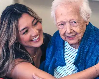 Young woman embracing elderly woman in a cozy setting, reflecting love and connection in a memory care environment.