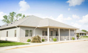 Savoy Place memory care facility in Savoy, IL, featuring a welcoming exterior with a porch, landscaped surroundings, and clear blue sky.