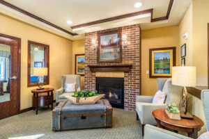 Cozy lobby area at Anthem Memory Care in Tinley Park, featuring comfortable seating, a brick fireplace, and decorative artwork, emphasizing a welcoming environment for residents and families.