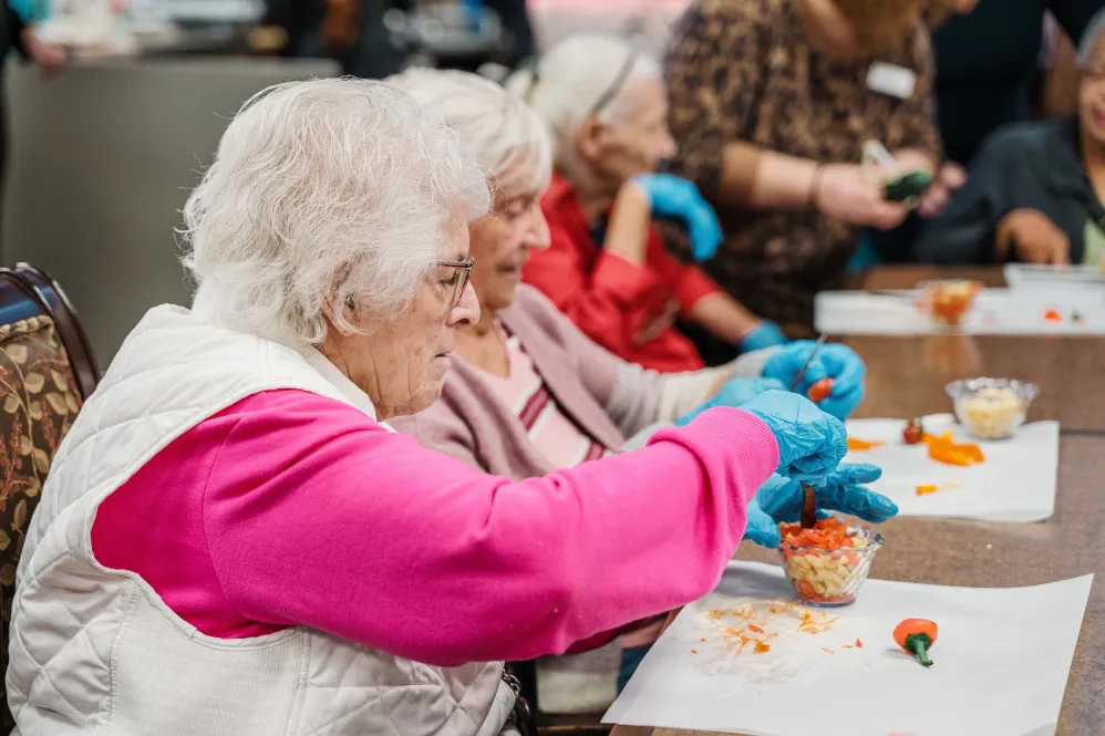 Residents of Willowbrook Place engaged in a community craft activity, preparing colorful ingredients in a supportive environment, promoting cognitive engagement and social interaction.