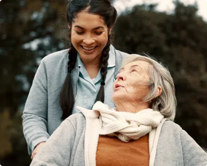 Caregiver smiling while assisting elderly woman in wheelchair, reflecting compassionate support in memory care environment.