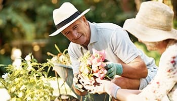 Man and woman gardening together, smiling, surrounded by greenery, showcasing community engagement and therapeutic activities at Chisholm Place Memory Care in Wichita.