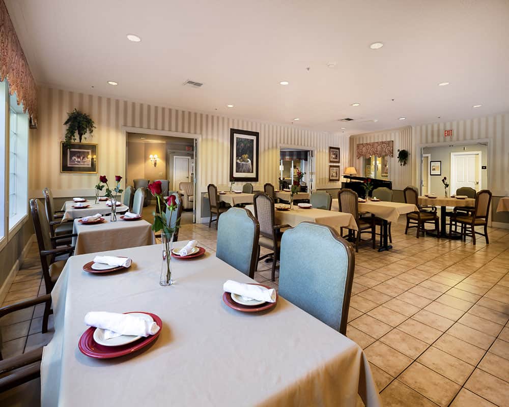 Dining area in Willow Springs Alzheimer's Special Care Center, featuring neatly set tables with red plates and white napkins, roses as centerpieces, and a warm, inviting atmosphere.