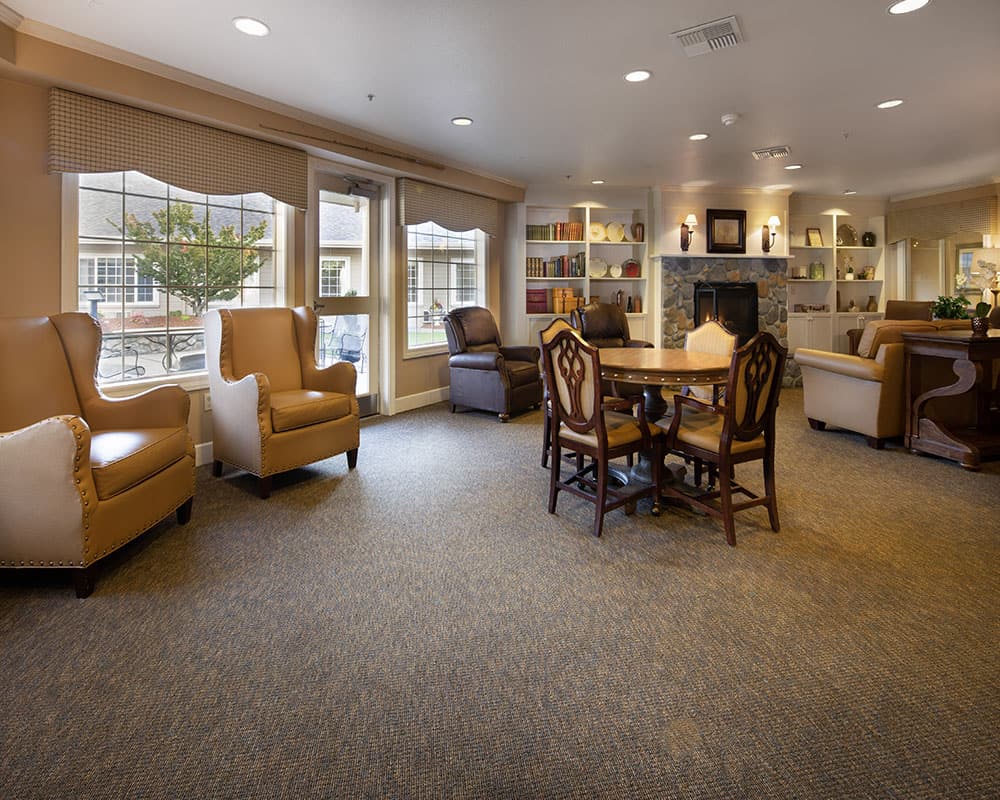Comfortable seating area in Willow Springs Alzheimer's Special Care Center, featuring brown leather chairs, a round table, and a cozy fireplace, designed for community interaction and memory care activities in Redding, CA.